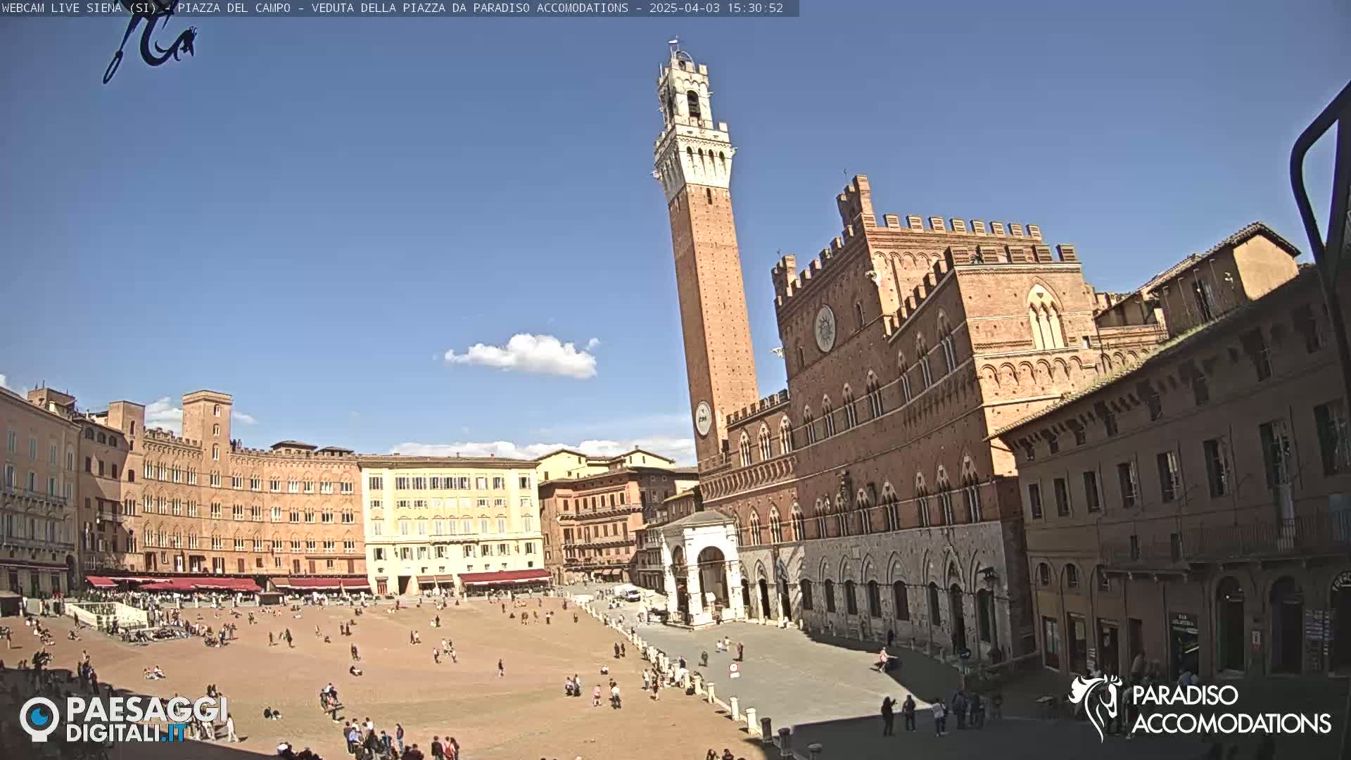 A large, mostly empty plaza is surrounded by brick buildings under a mostly sunny sky with a few clouds.