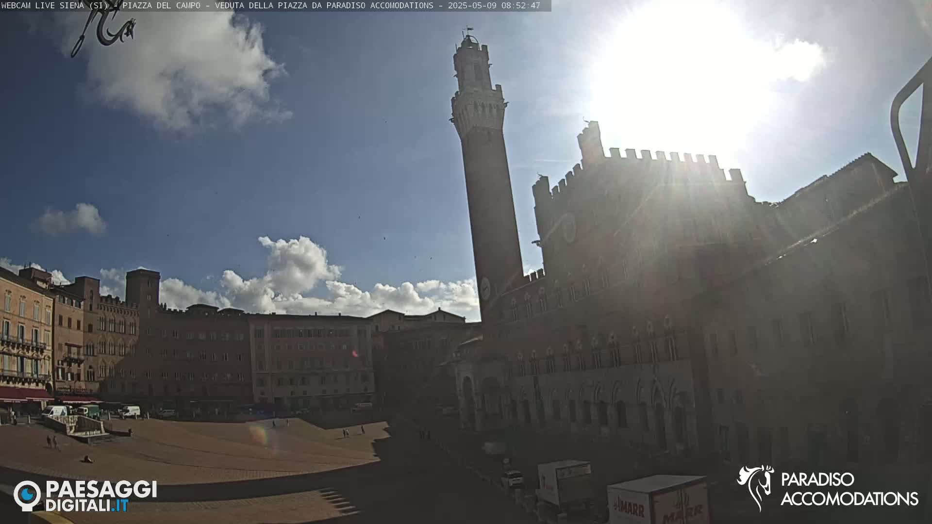 A sunny day reveals a large, open plaza surrounded by historic brick buildings, one prominently featuring a tall tower.