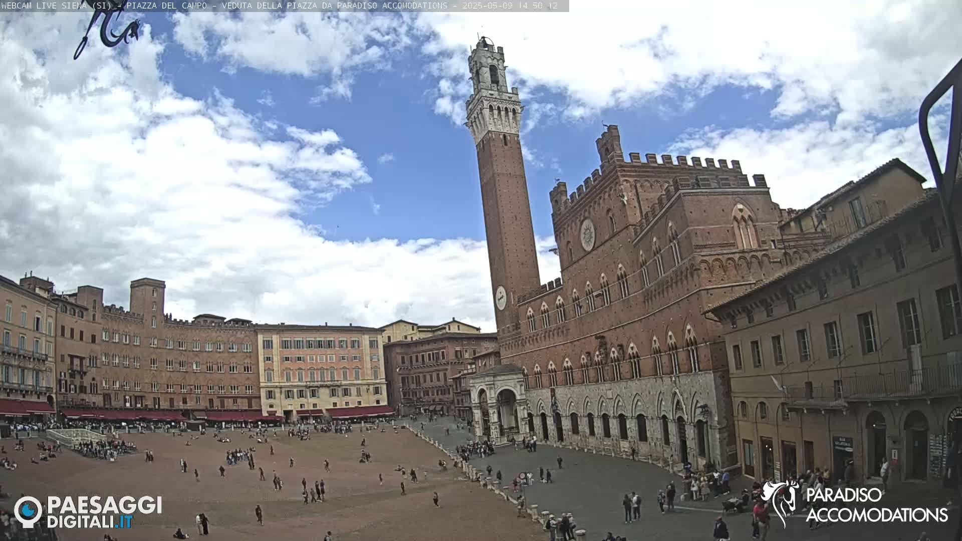 A large, mostly empty plaza is surrounded by red-brick medieval buildings under a partly cloudy sky.
