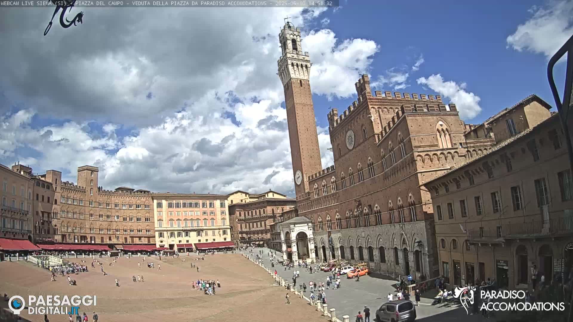 A large, brick piazza in Siena, Italy, is filled with people under a partly cloudy sky.