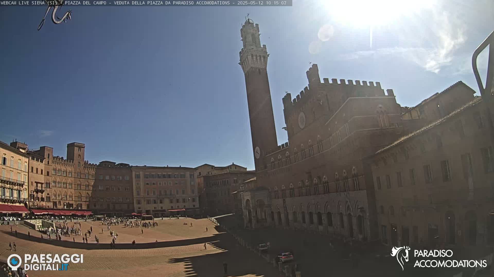 A sunny day in a large, open square surrounded by brick buildings, including a tall tower and a large palazzo.