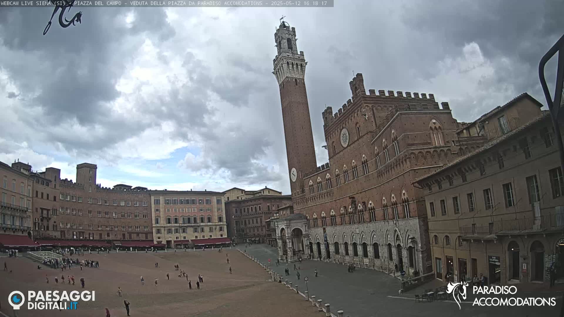 A large, brick piazza in Italy is mostly empty under a partly cloudy sky.
