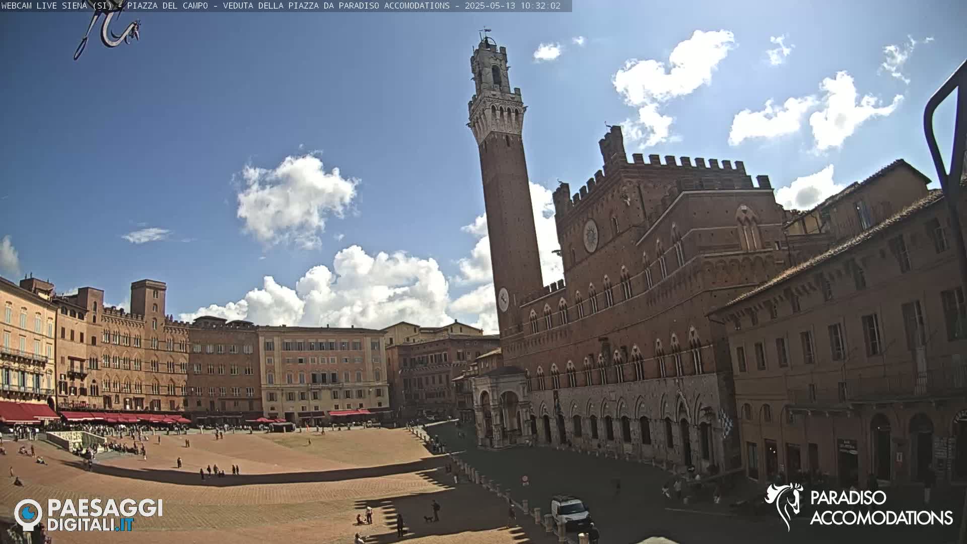 A large, brick public square in Siena, Italy, is mostly empty under a partly cloudy blue sky.
