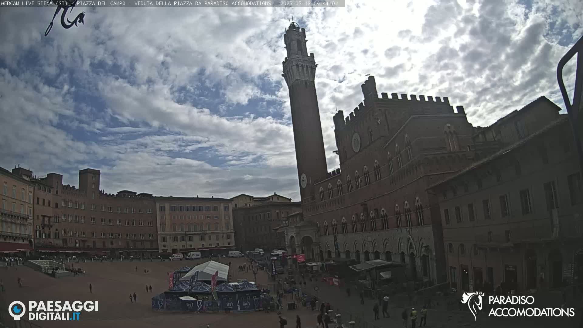 A large, mostly empty town square is surrounded by historic brick buildings under a partly cloudy sky.