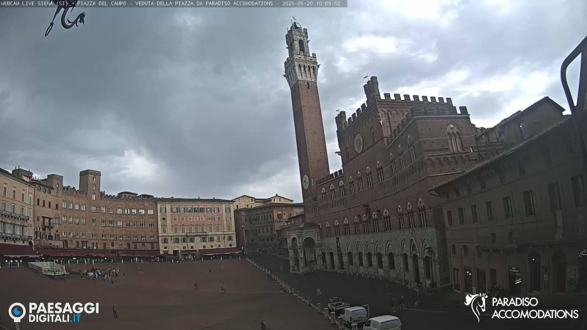 A large, brick piazza in Siena, Italy, is shown under a mostly cloudy sky, with the Torre del Mangia and Palazzo Pubblico prominently featured.