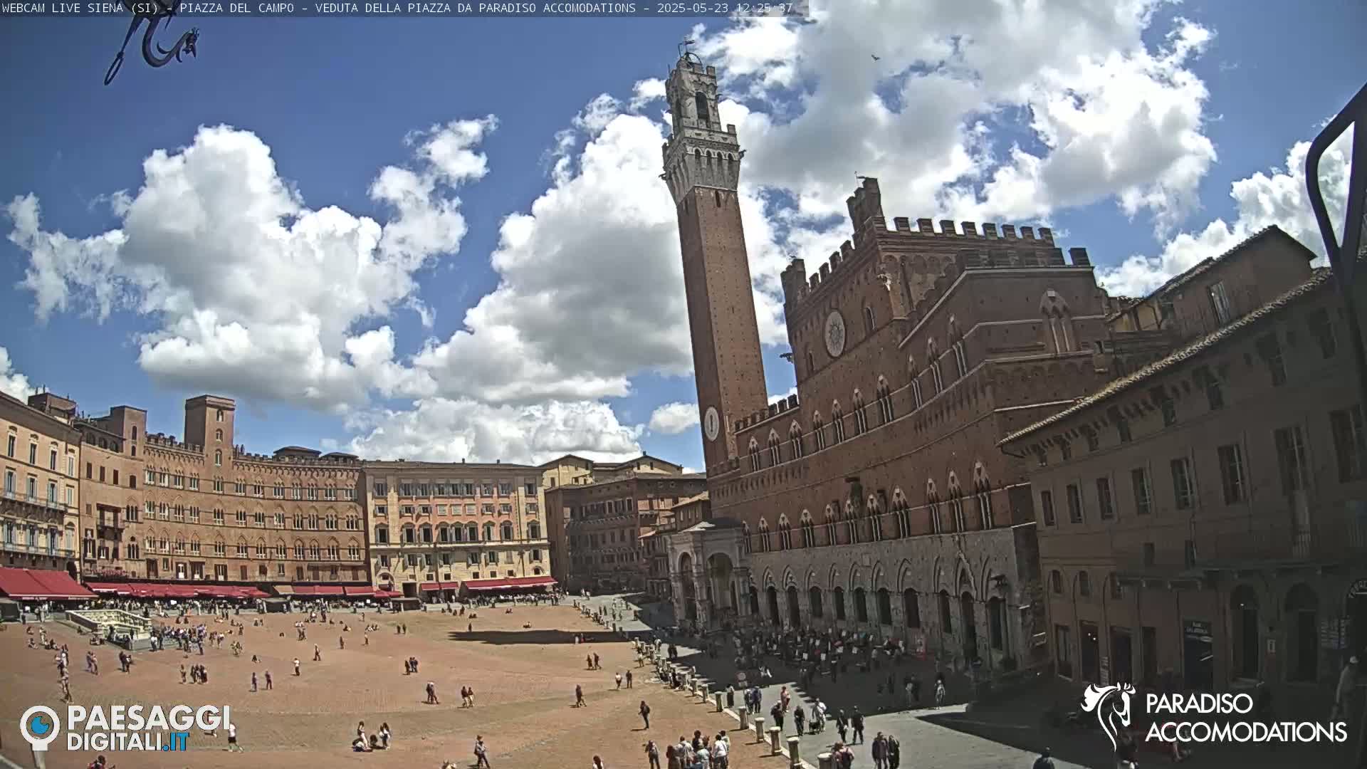 A large, brick plaza with numerous buildings and a tall tower under a partly cloudy sky.