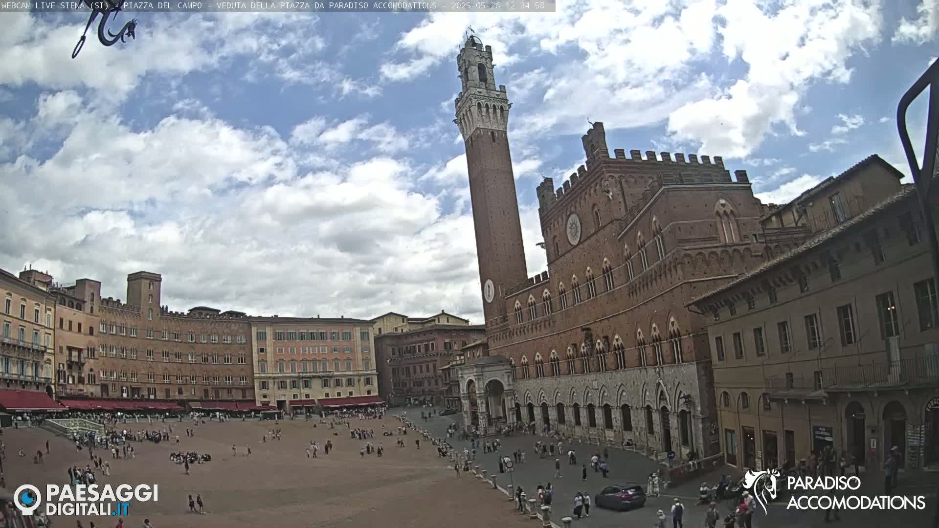 A large, brick piazza with a tall tower and surrounding buildings under a partly cloudy sky.