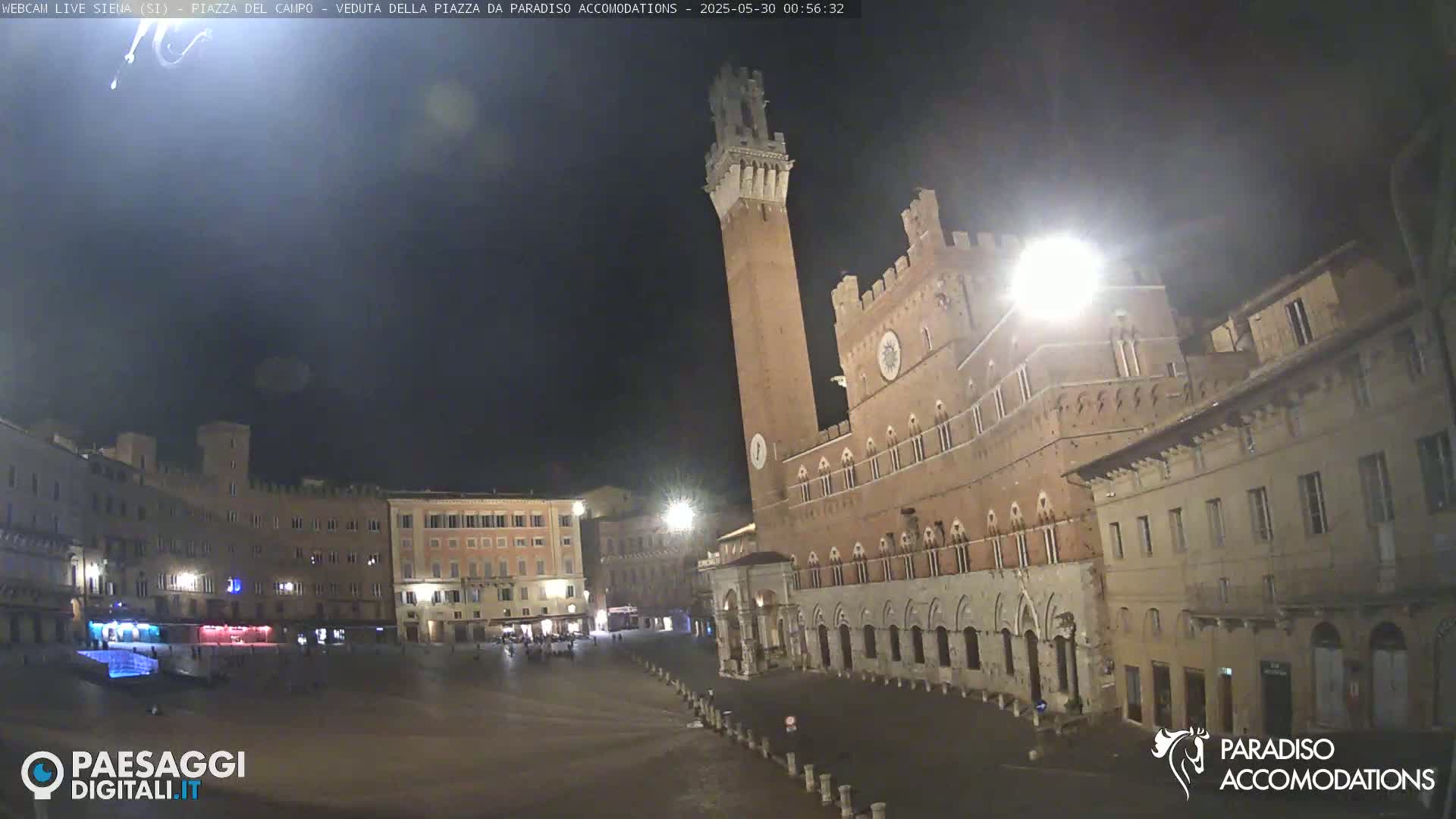 A nighttime view of a large, mostly empty, town square with a tall brick tower and surrounding buildings.