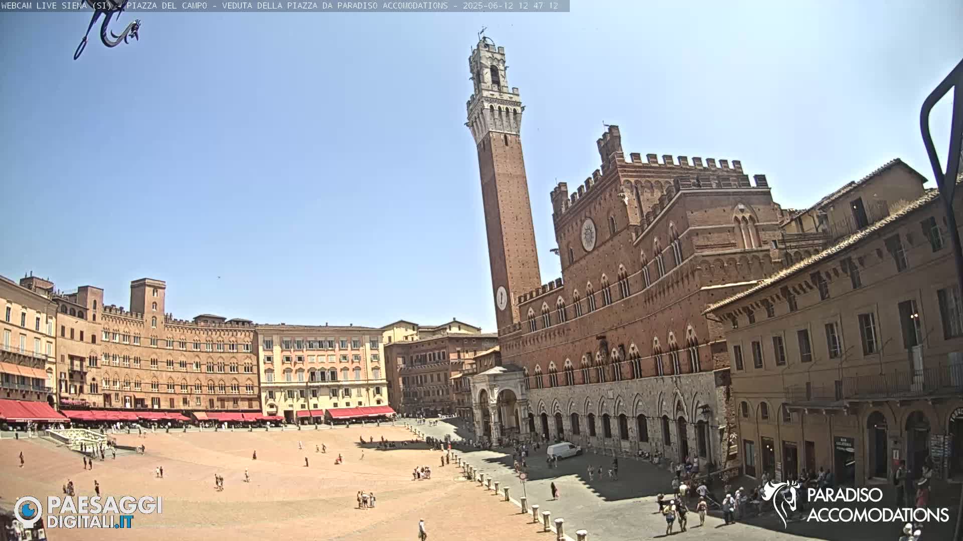 A large, brick public square in Siena, Italy, is filled with people on a sunny day, with the Palazzo Pubblico and Torre del Mangia prominently featured.