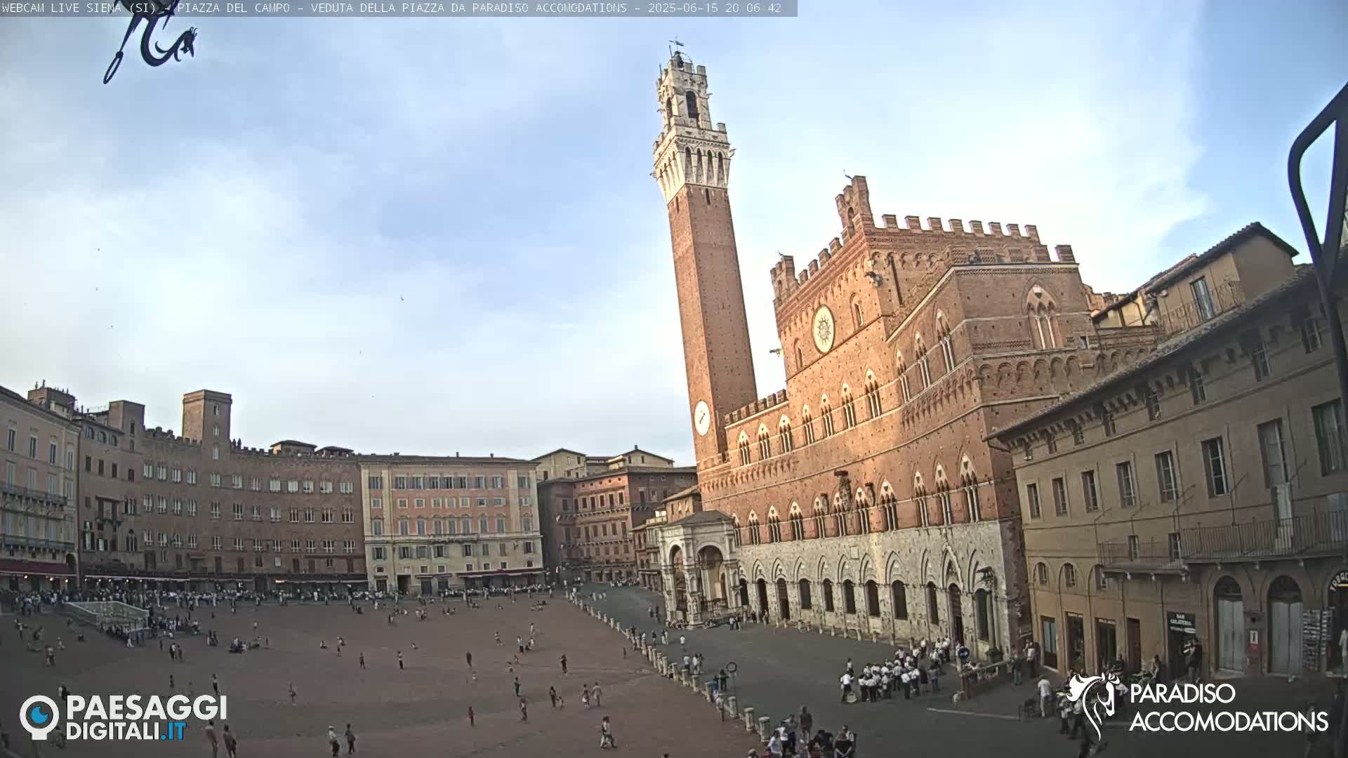 A large, brick plaza in Siena, Italy, is sparsely populated under a mostly clear, light-blue sky.