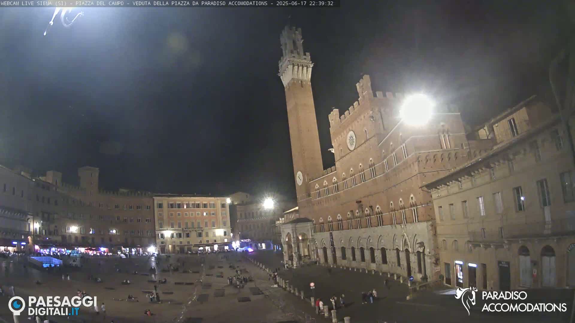 A nighttime view of a large, mostly empty town square with a tall brick tower and adjoining buildings.