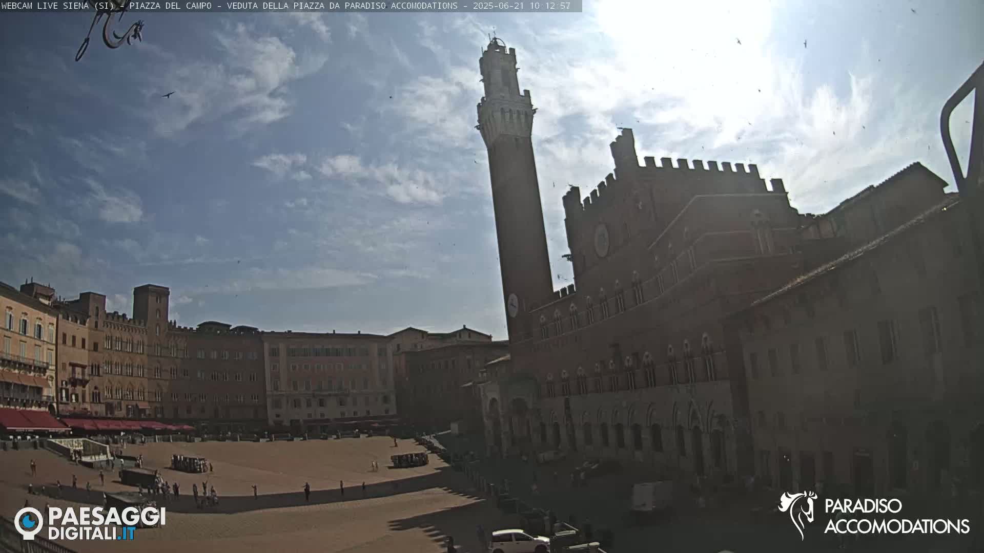 A sunny day reveals a large, empty plaza surrounded by historic brick buildings, one prominently featuring a tall tower.