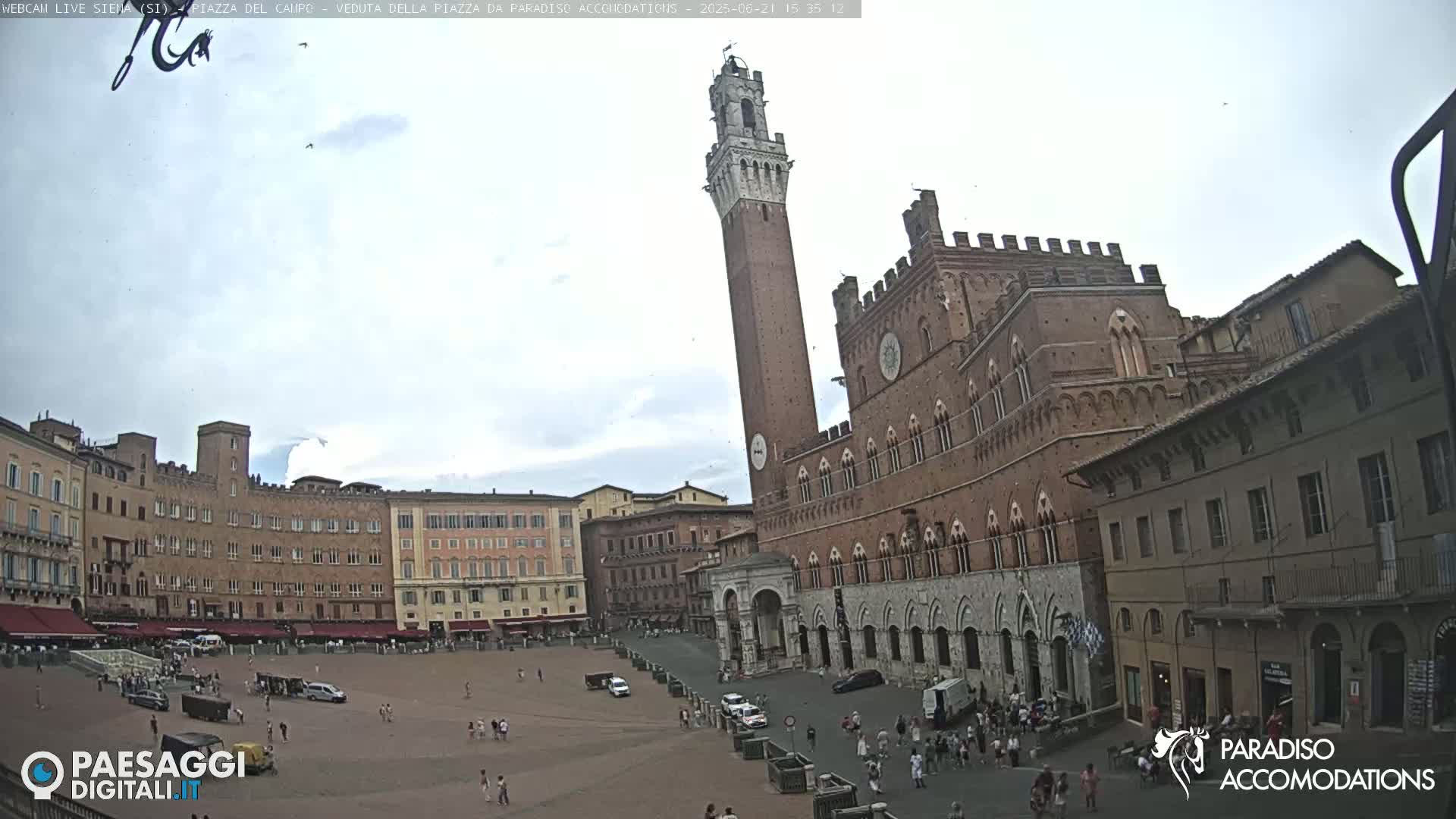 A large, brick public square with several buildings, including a tall tower and a large palace, under a partly cloudy sky.