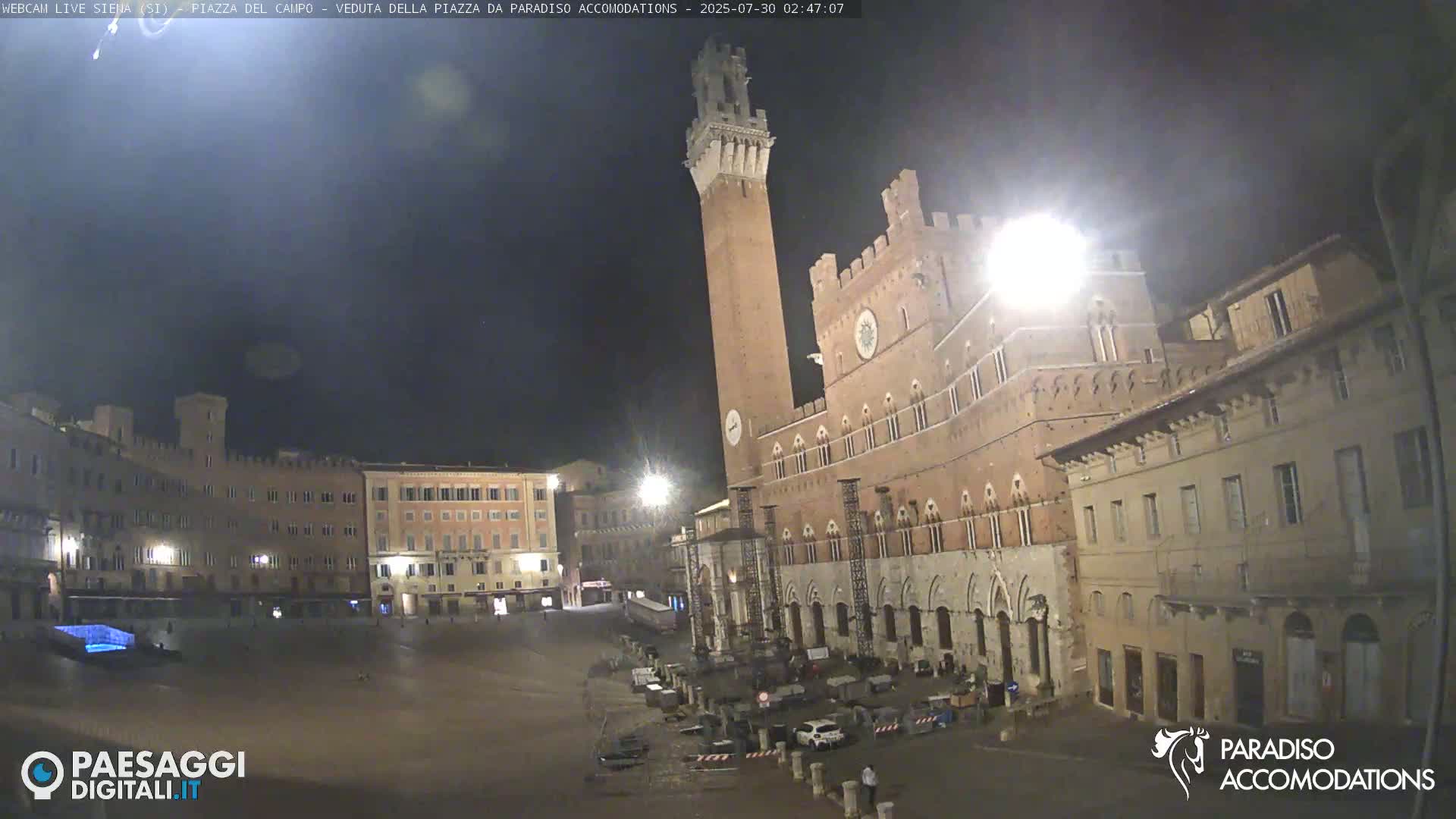 A sunny day reveals a large, mostly empty plaza surrounded by historic Italian buildings, including a tall tower and a large palace.