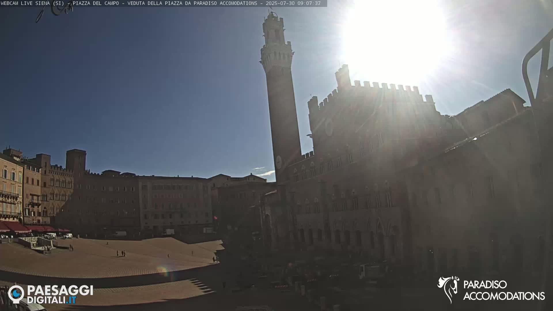A sunny day in a large, brick-paved plaza surrounded by historic buildings, including a tall tower.