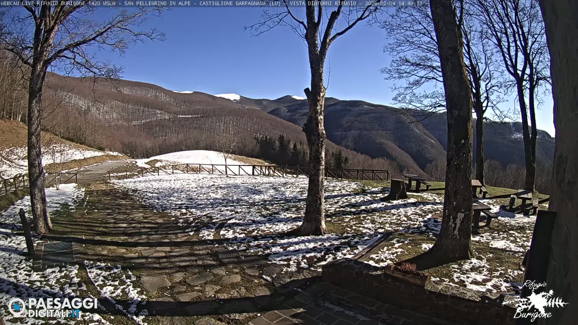 A snow-dusted stone patio with picnic tables sits in front of a mountain view under a clear blue sky.