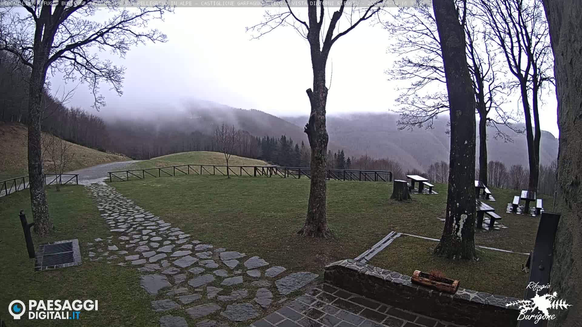 A stone path leads to several picnic tables situated on a grassy area overlooking fog-shrouded mountains.
