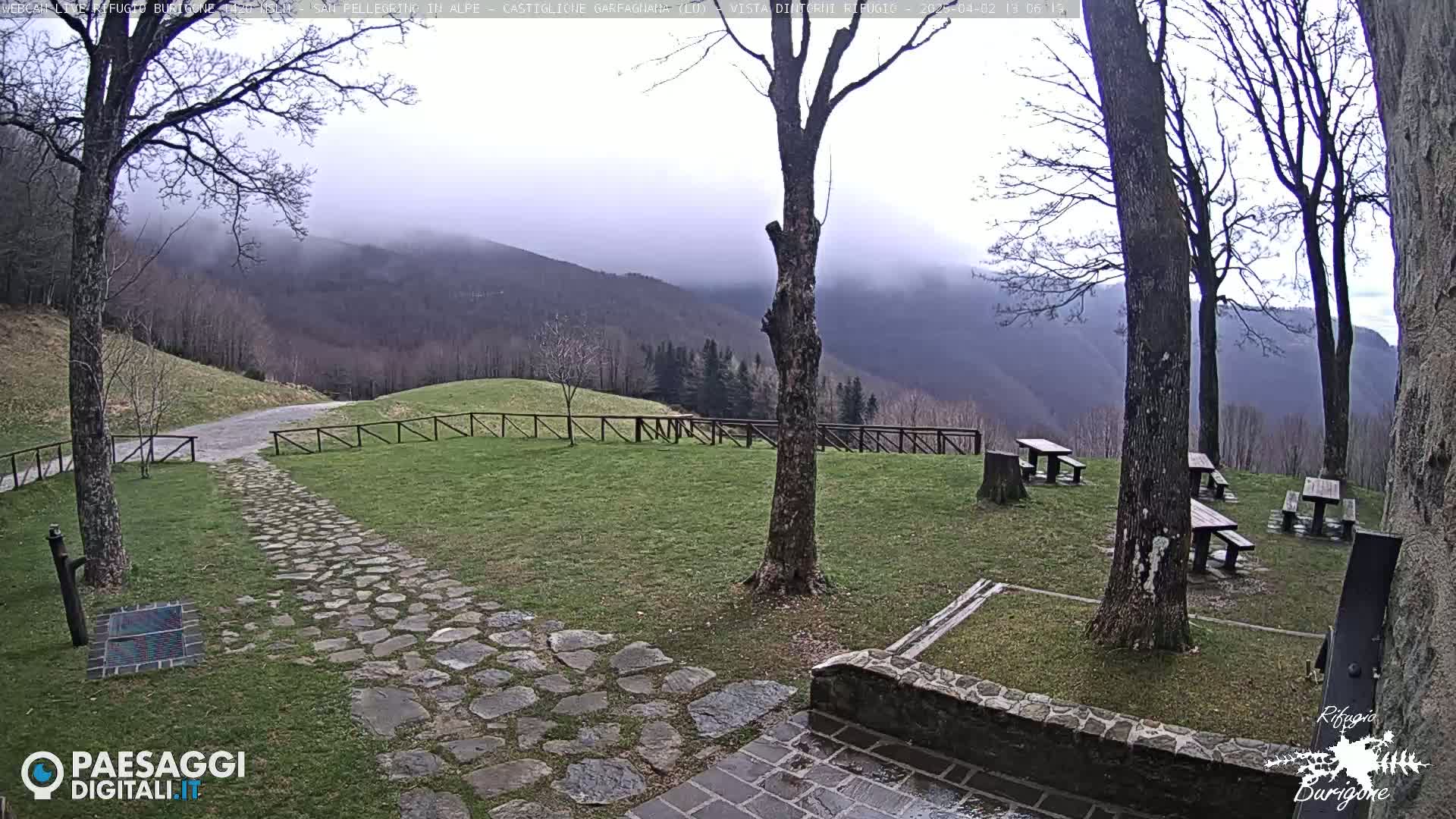 A stone path leads to picnic tables situated on a grassy area overlooking misty mountains under an overcast sky.