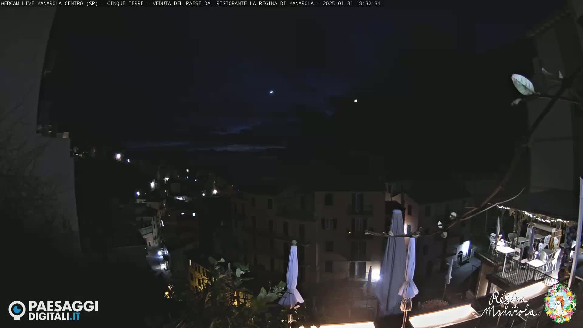 A nighttime view of a village nestled on a hillside, illuminated by scattered lights under a dark, mostly clear sky.