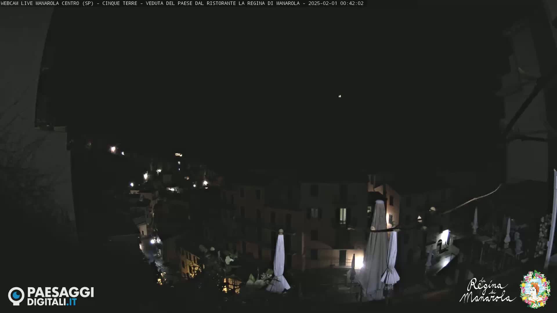 A nighttime, high-angle view of a village nestled on a hillside, with closed umbrellas visible in the foreground.
