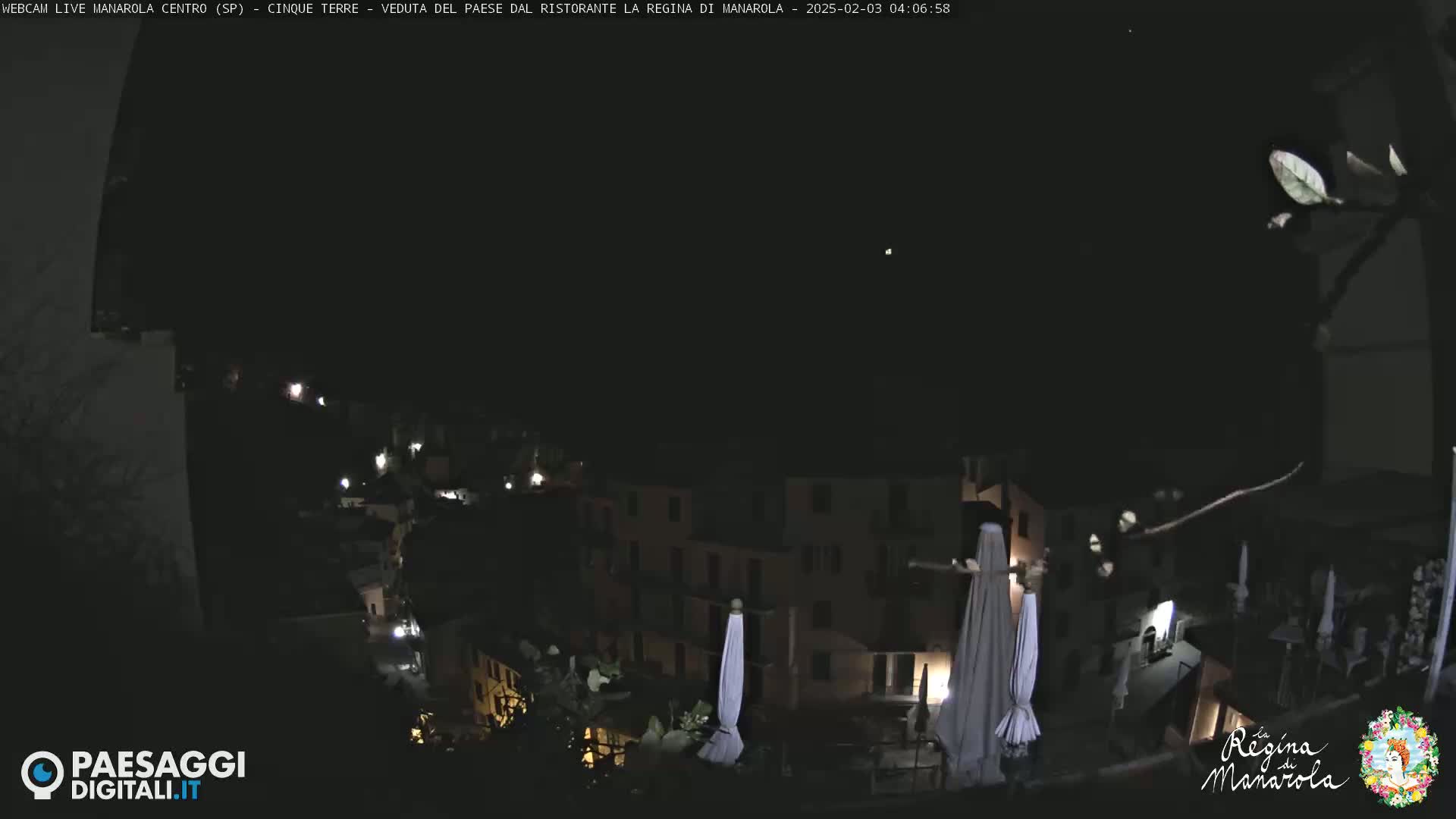 A nighttime, long shot of a village nestled on a hillside, with a few lights visible and closed umbrellas in the foreground.