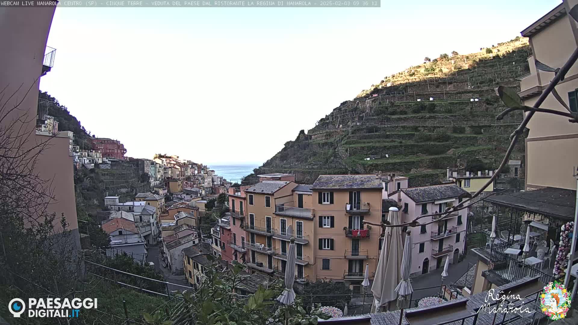 A hilly coastal town with colorful buildings clings to a steep hillside overlooking the sea under a mostly clear sky.