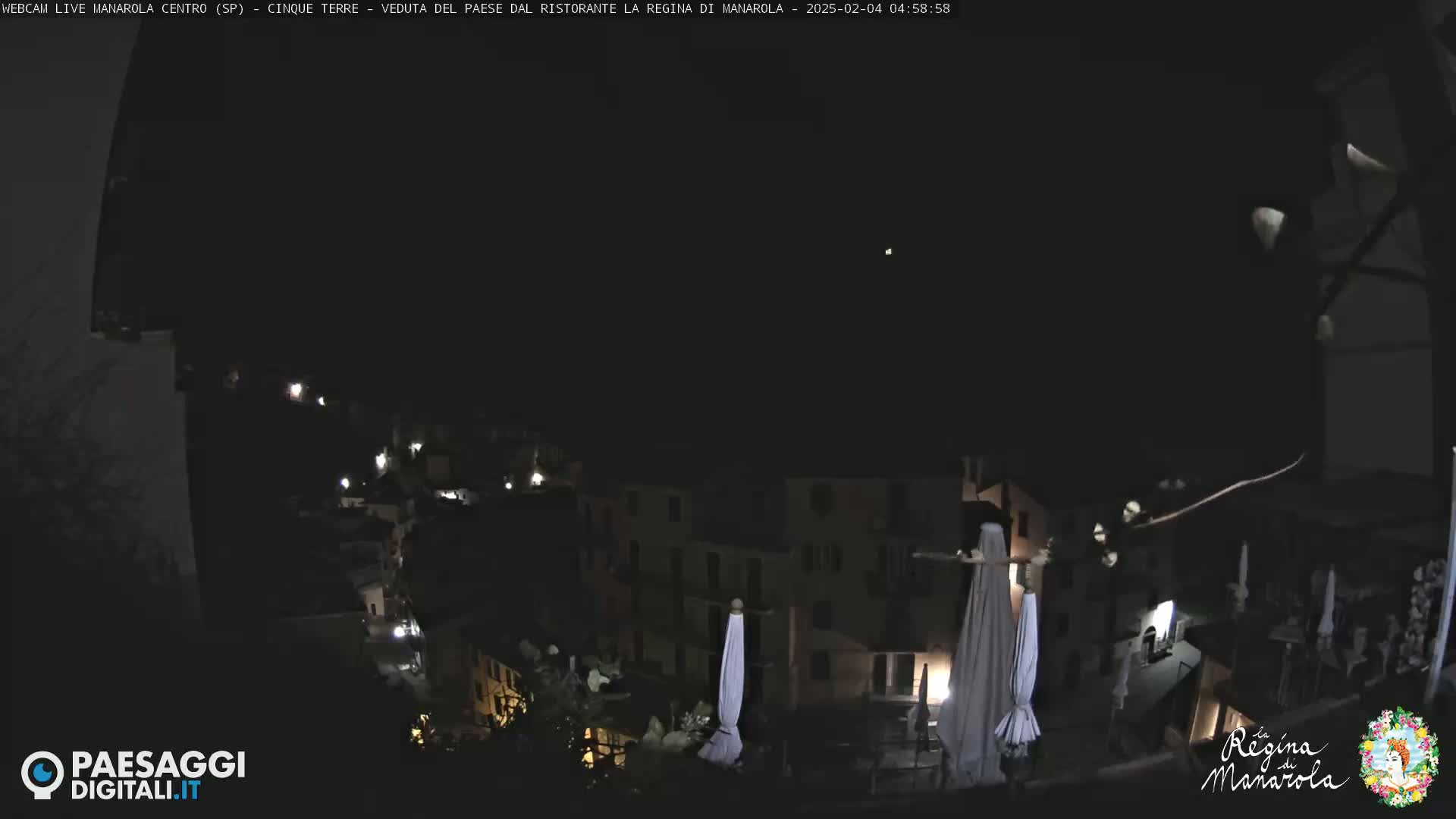 A nighttime, long shot of a village nestled on a hillside, with several lights illuminating buildings and closed umbrellas.