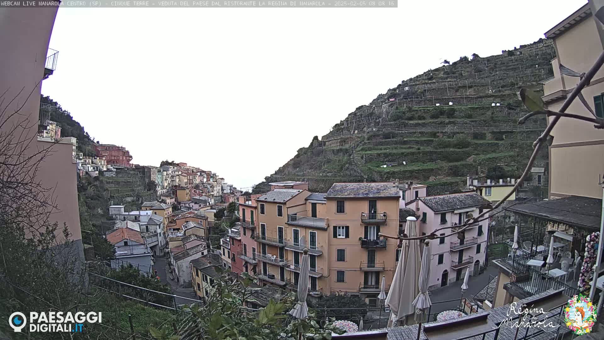 A hillside village of colorful buildings climbs a steep, terraced mountainside under an overcast sky.