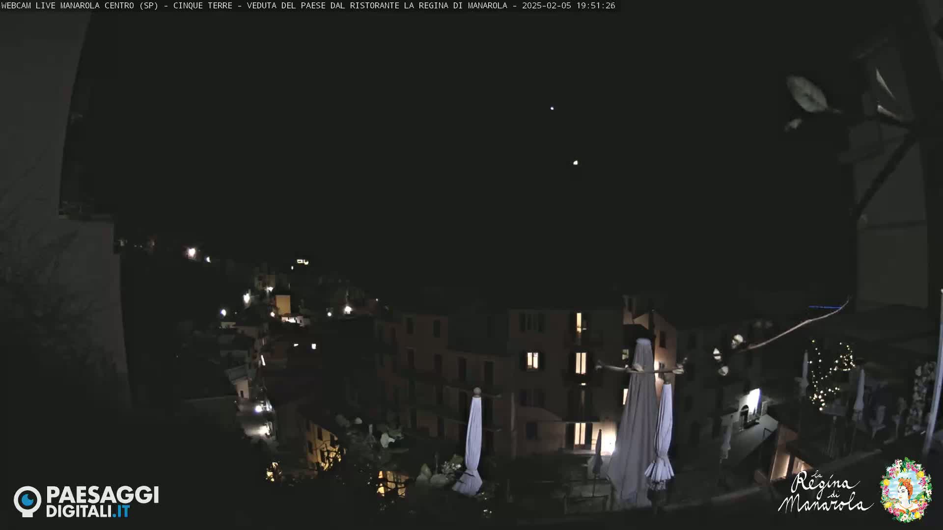 A nighttime, clear-sky view of a hillside town with illuminated buildings and closed umbrellas.