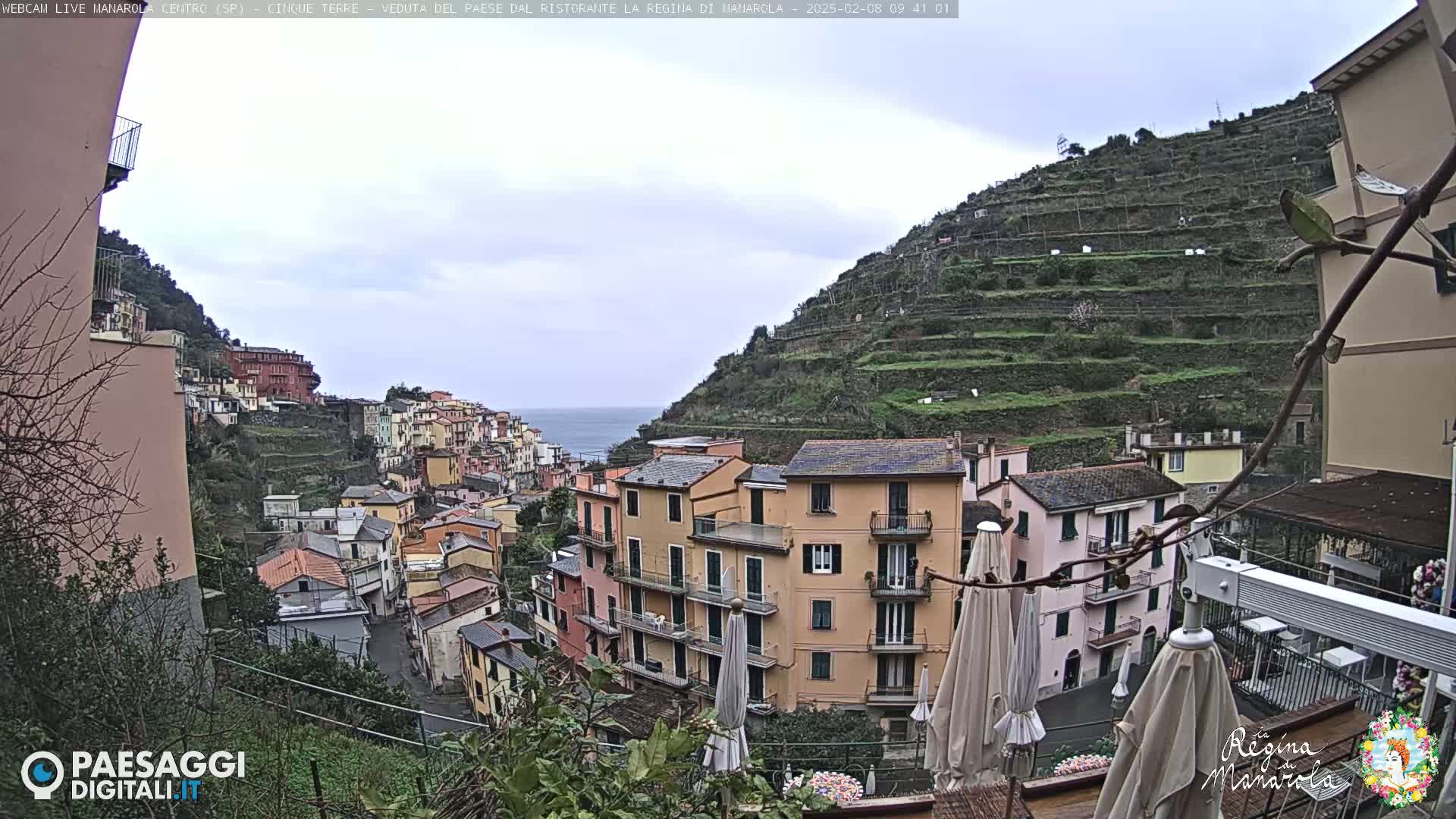 A hillside village of colorful buildings overlooks a calm sea under an overcast sky.