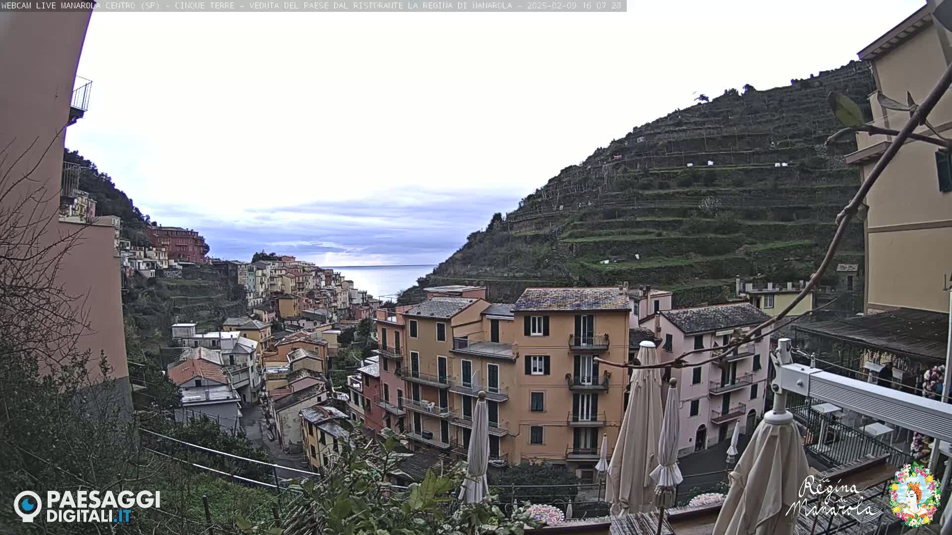 A hillside village of colorful buildings overlooks a calm sea under an overcast sky.
