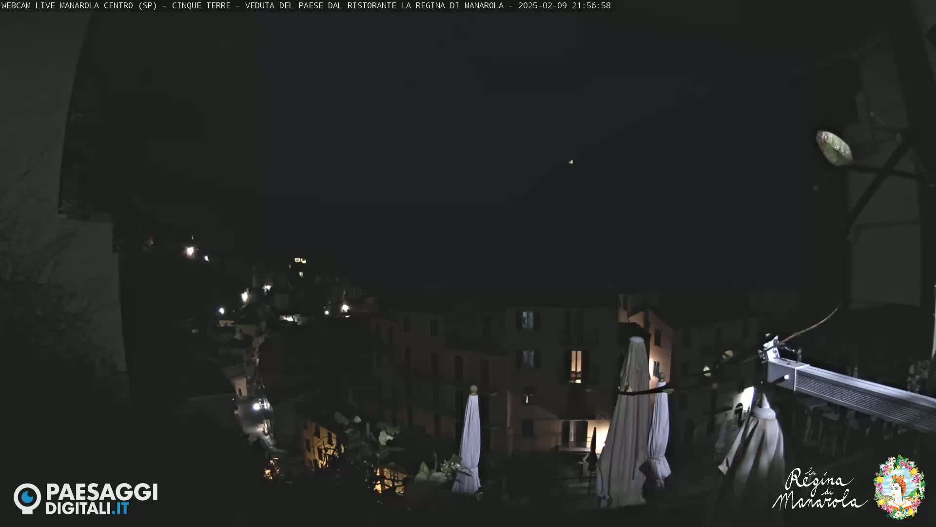 A nighttime view of a town nestled on a hillside, with several closed umbrellas visible in the foreground.