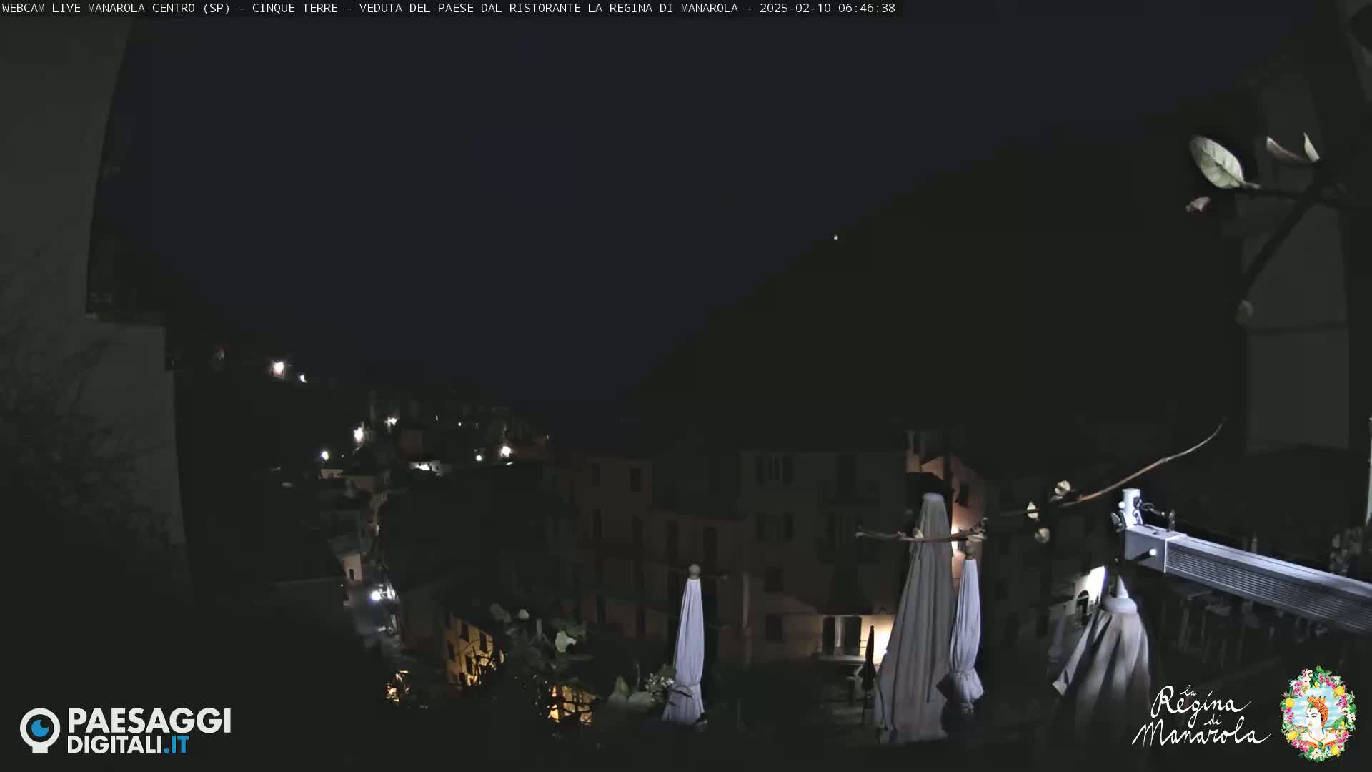 A nighttime view of a village nestled on a hillside, with closed umbrellas and dim lights visible, under a dark sky.