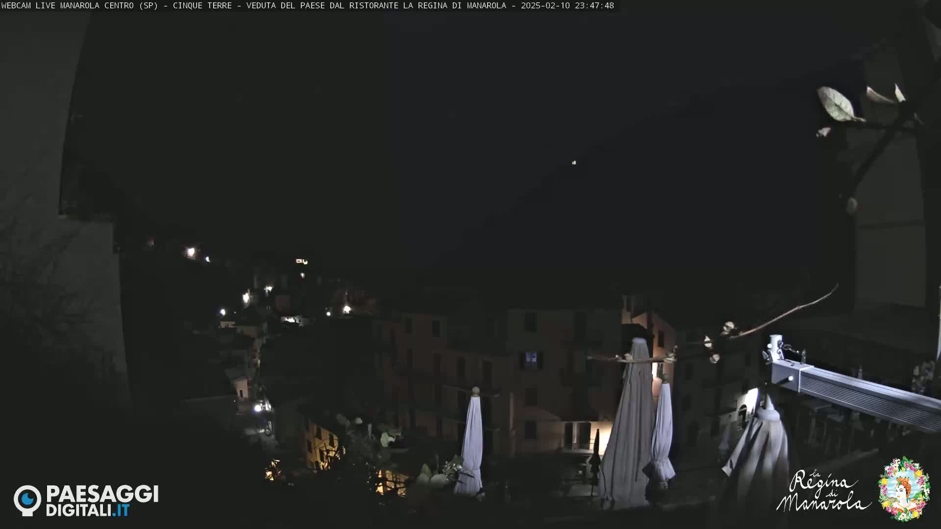 A nighttime view of a town nestled on a hillside, illuminated by scattered lights under a clear, dark sky.