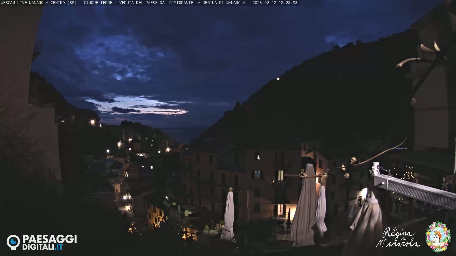 A nighttime view of a hillside village with sparsely lit buildings, under a mostly dark sky with a hint of twilight.