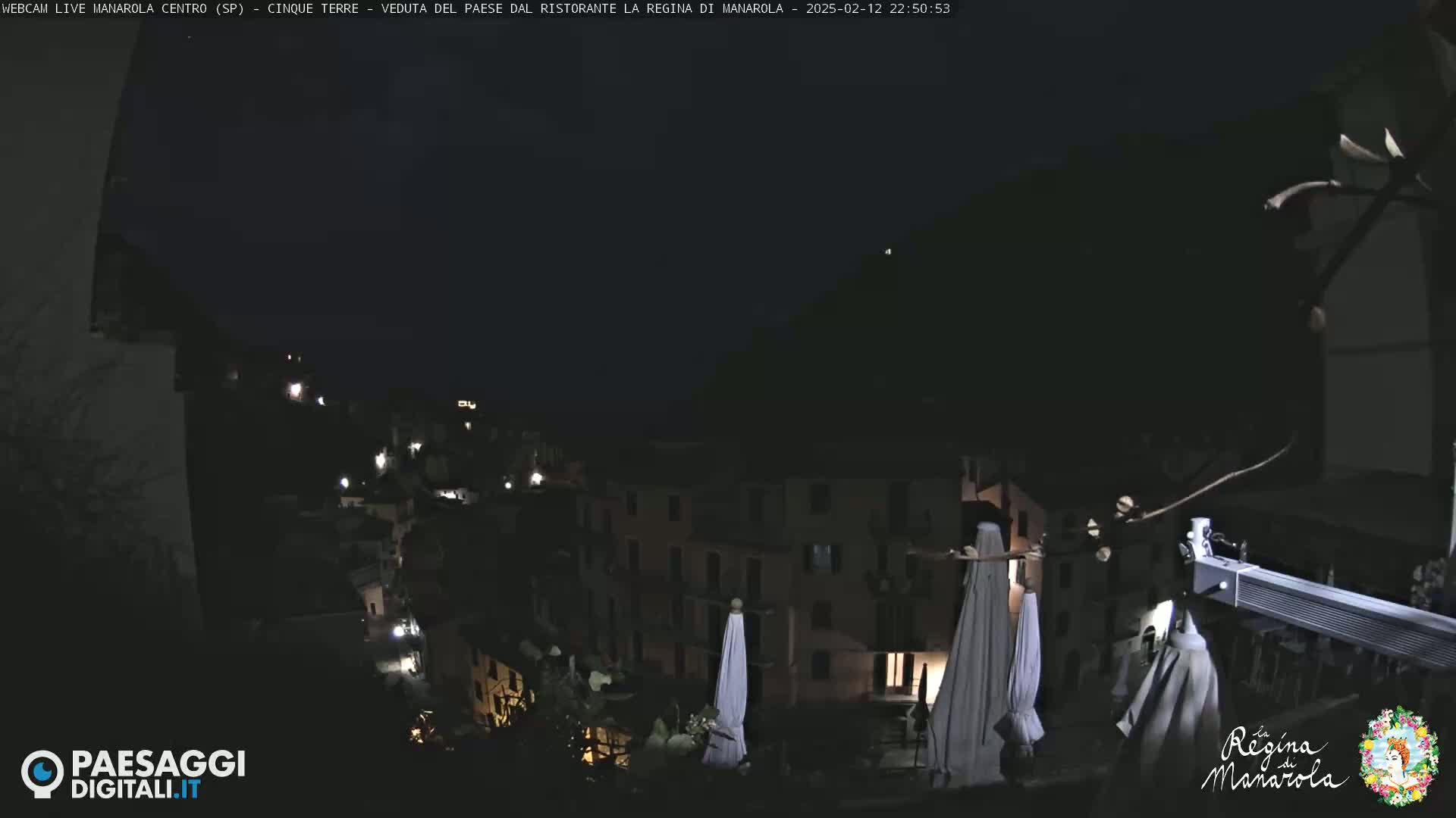 A nighttime view of a village nestled on a hillside, illuminated by scattered lights under a dark sky.