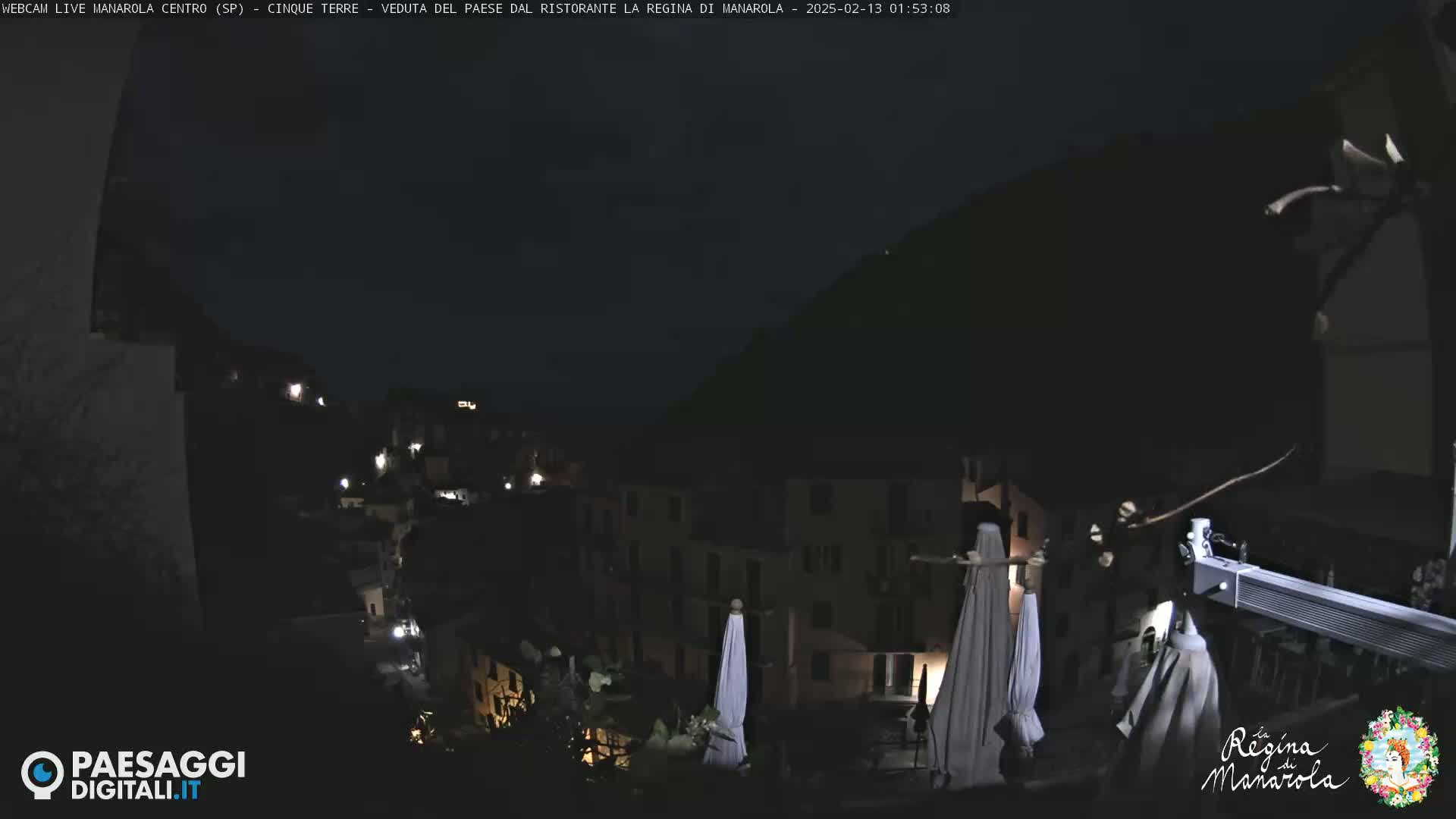 A nighttime view of a village nestled on a hillside, with closed umbrellas and faint lights visible.