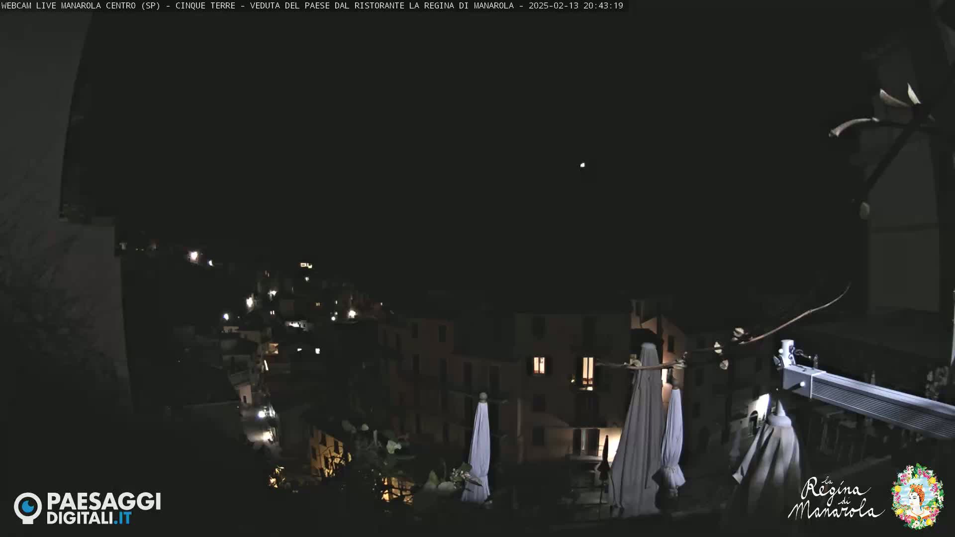 A nighttime, clear-sky view of a small, dimly lit town nestled on a hillside, with several closed patio umbrellas visible in the foreground.