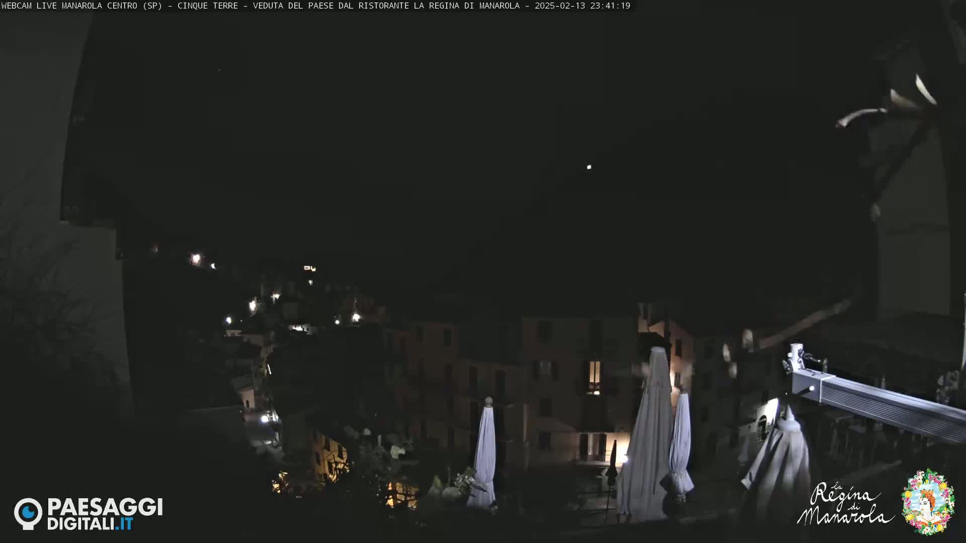 A nighttime view of a village nestled on a hillside, with several closed umbrellas visible in the foreground.