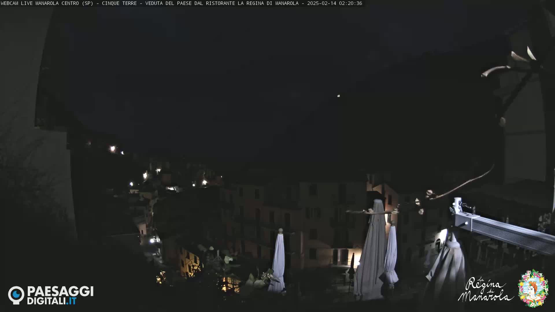 A nighttime, dark view of a town nestled on a hillside, with some lights visible and several closed umbrellas.