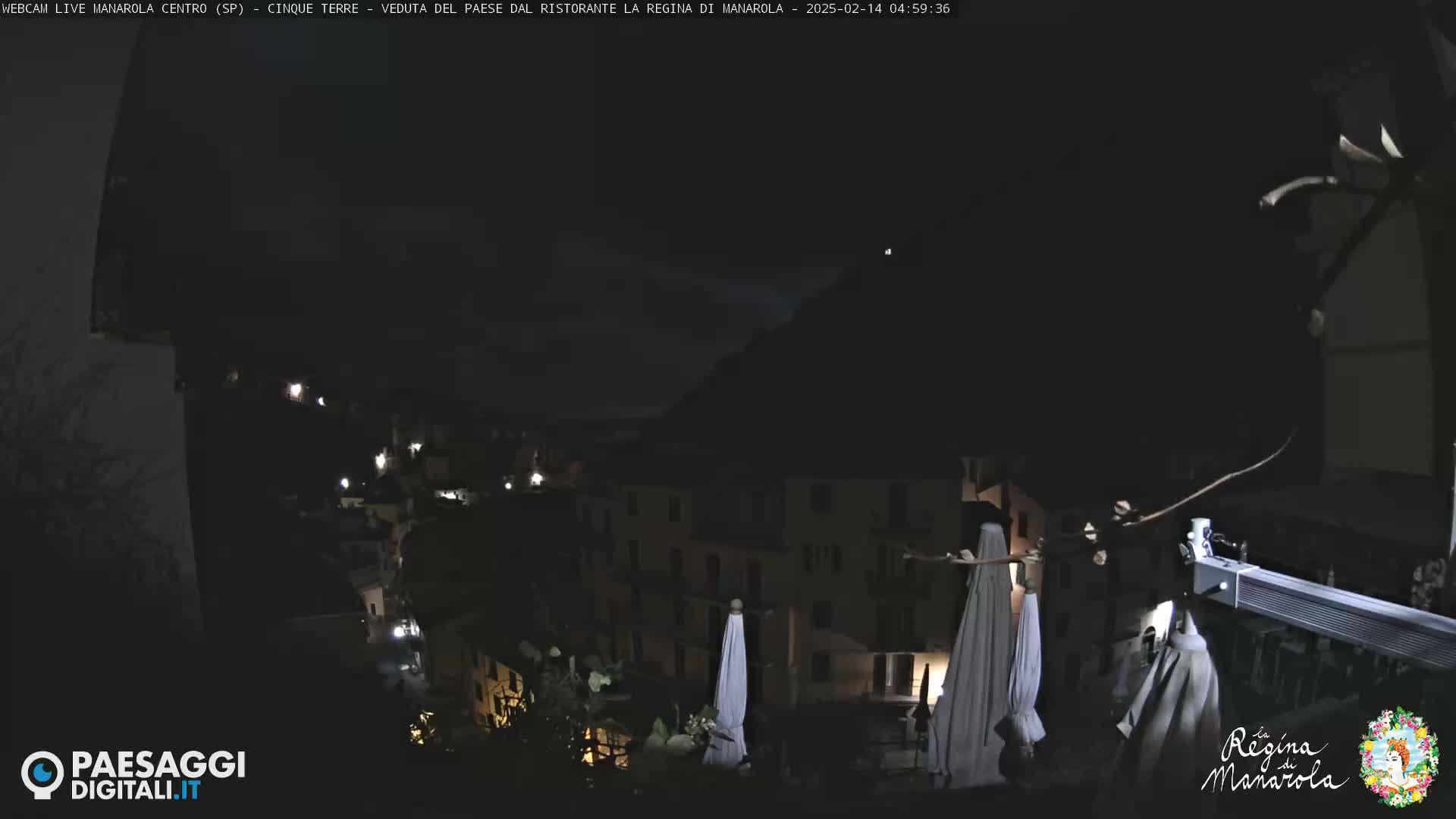 A nighttime view of a dark, hilly town with a few lights visible, and several closed white umbrellas on a balcony.