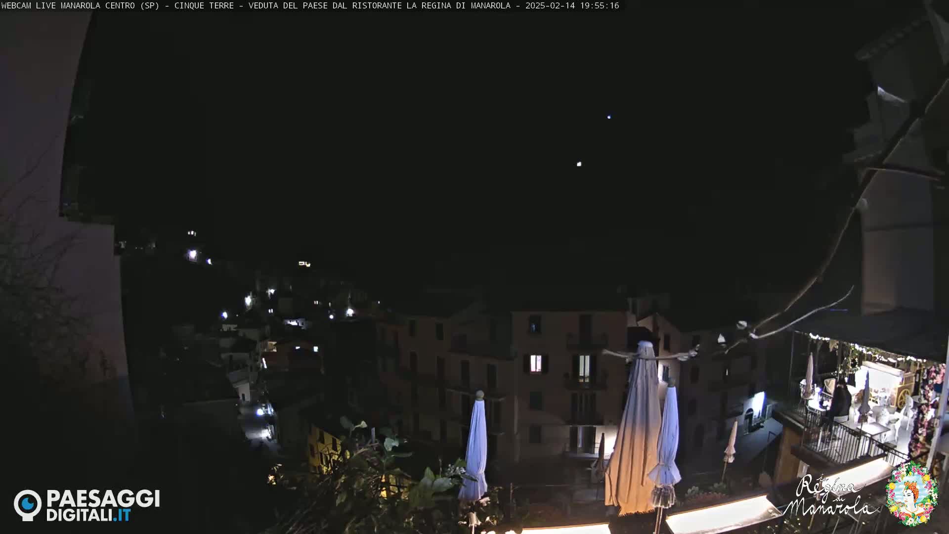 A nighttime view of a village nestled on a hillside, illuminated by scattered lights, under a clear, dark sky.