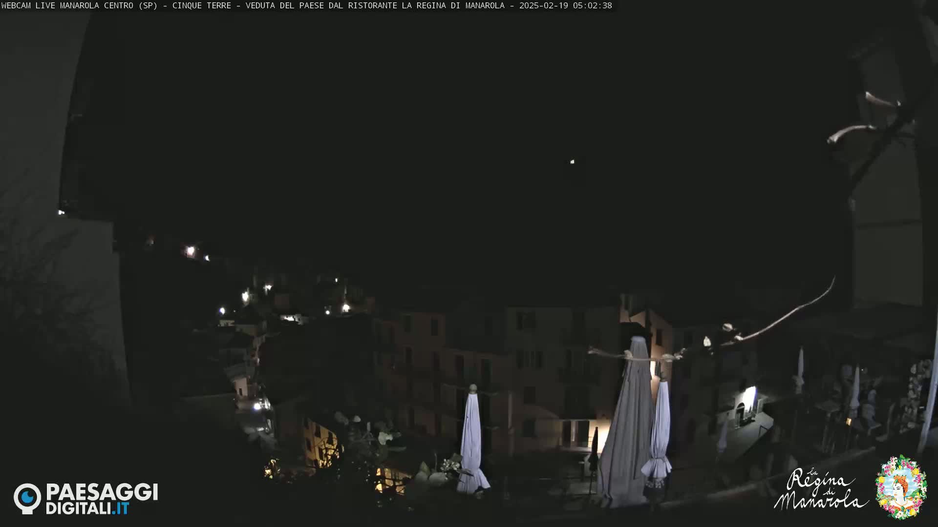 A nighttime, dark view of a village nestled on a hillside, with a few lights visible and closed umbrellas.