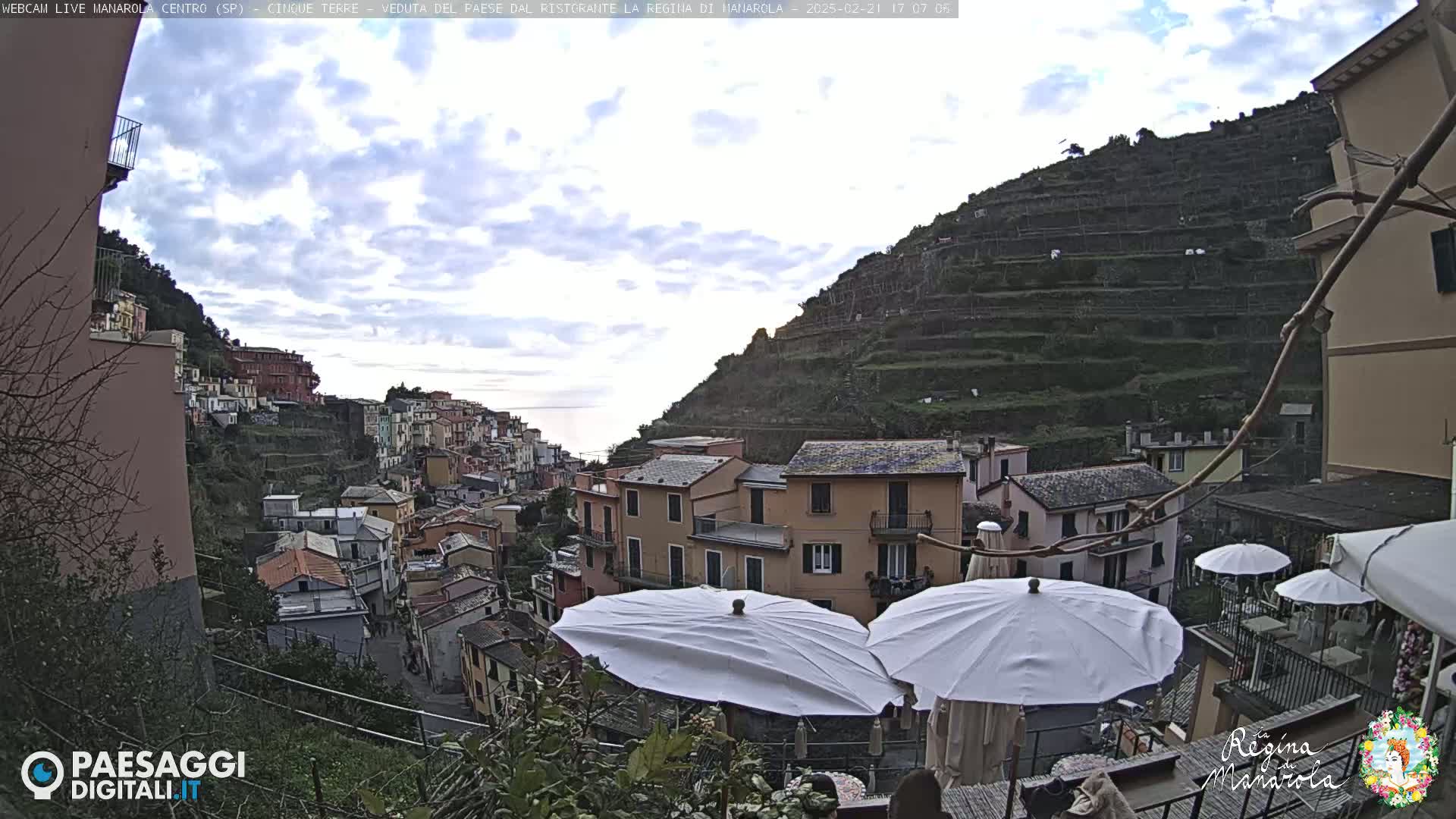 A cloudy day overlooking a colorful hillside village with terraced gardens, partially obscured by patio umbrellas.