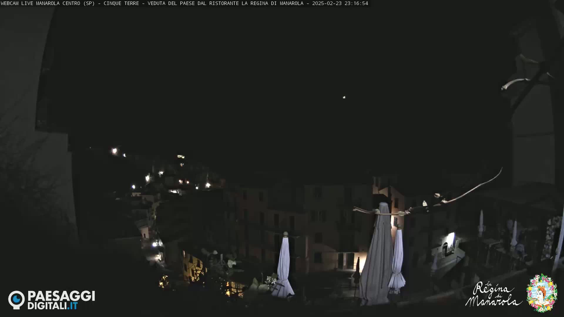 A nighttime view of a village with dimly lit buildings and closed umbrellas, under a clear, dark sky.
