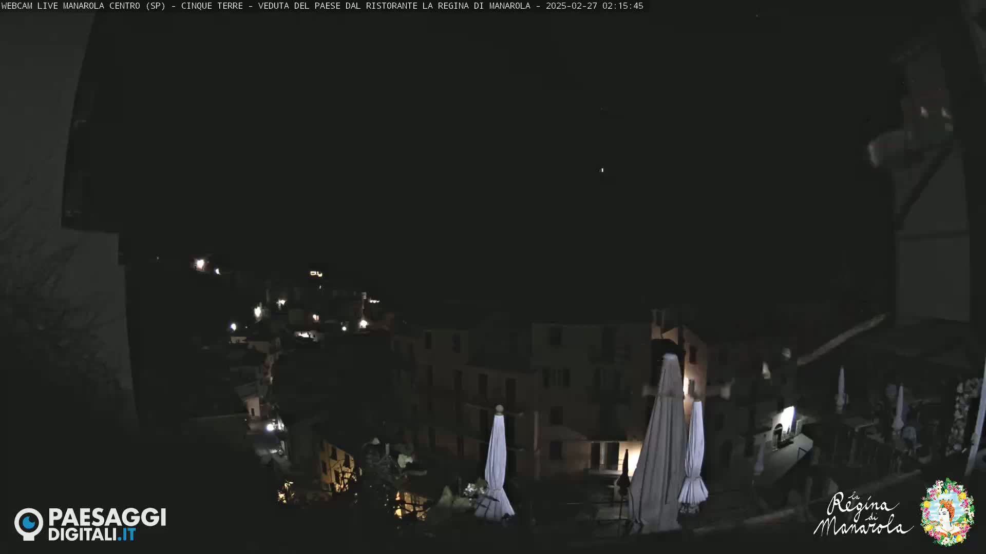 A nighttime view of a hillside town with buildings illuminated by scattered lights, under a dark, clear sky.