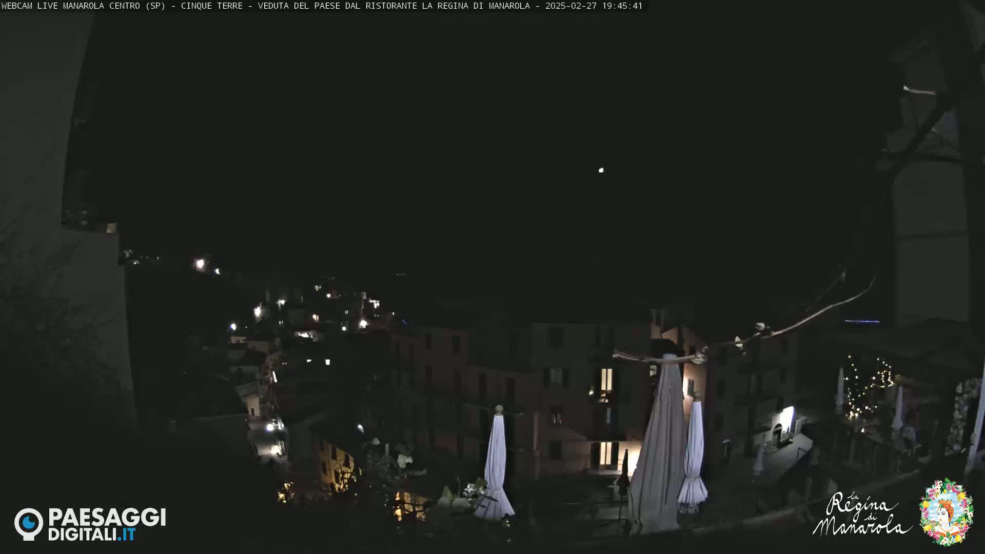 A nighttime view of a village with illuminated buildings and closed umbrellas, under a clear, dark sky.