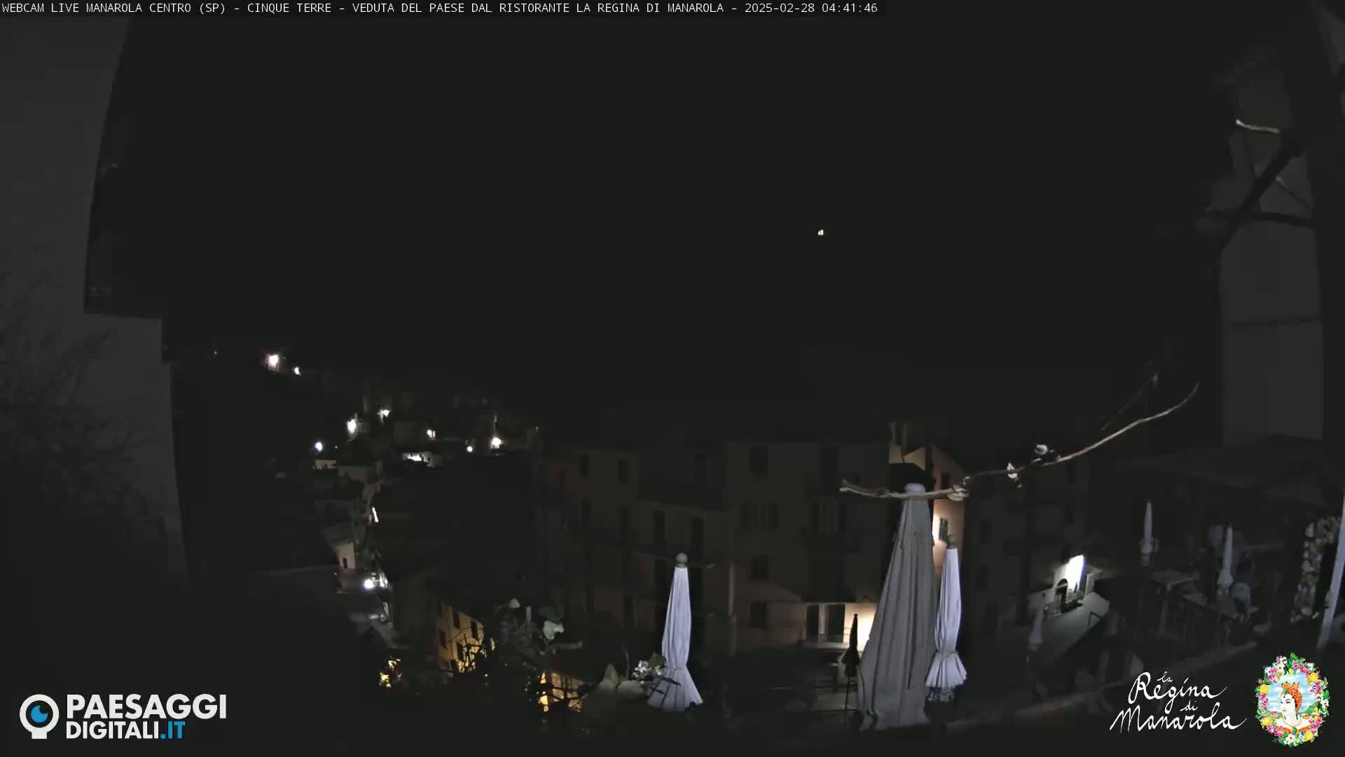 A nighttime view of a dimly lit town nestled on a hillside, with several closed umbrellas visible in the foreground under a dark sky.