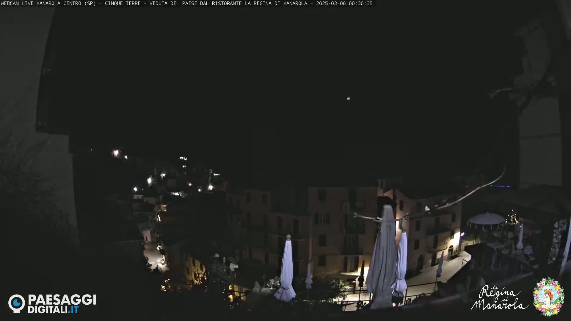 A nighttime, high-angle view of a town, possibly in Italy, with closed umbrellas and some lights visible in the buildings.