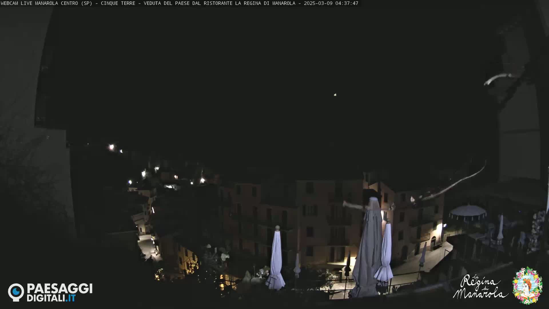 A nighttime view of a small town nestled on a hillside, with several closed umbrellas visible on a rooftop.
